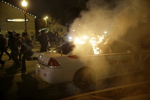 Hořící policejní vůz při protestech ve Fergusonu.